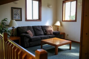 A living room with a dark sofa, two lamps, a wooden coffee table, and a painting on the wall. - Lakefront Cabin Rental with a Paddle Boat near Wisconsin Dells, Wisconsin (Tomah)
