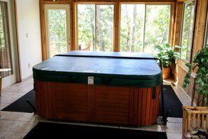 A hot tub in a room with large windows, a wooden floor, and a black mat. - Lakefront Cabin Rental with a Paddle Boat near Wisconsin Dells, Wisconsin (Tomah)