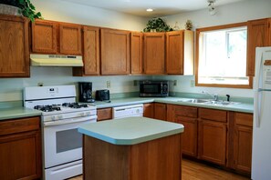 A kitchen with wooden cabinets, a stove, a microwave, a sink, and a window. - Lakefront Cabin Rental with a Paddle Boat near Wisconsin Dells, Wisconsin (Tomah)