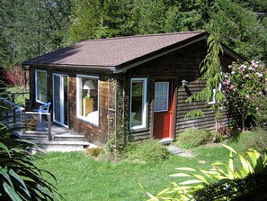 Une petite cabane en bois avec un porche, une porte rouge et une porte vitrée donnant sur un espace patio.