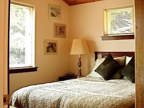 Ein Schlafzimmer mit einem Bett, einem Nachttisch, einer Lampe und drei gerahmten Bildern an der Wand.