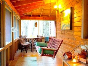 Un acogedor interior de cabaña con techo de madera, una silla colgante, una mesa de comedor con sillas y una chimenea.
