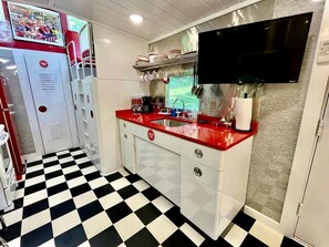A kitchen with a checkered floor, a red countertop, and a flat-screen TV mounted above the sink.