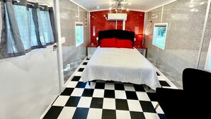 Una habitación con piso a cuadros, una cama con ropa blanca, un cabecero rojo y un ventilador de techo.