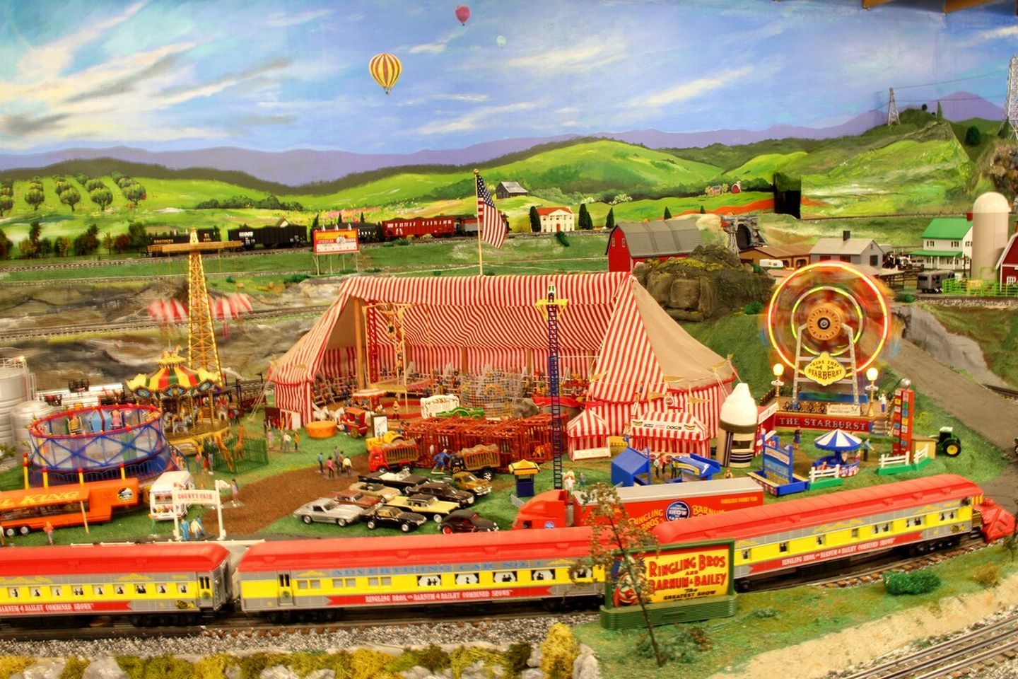 A model train set with a circus theme, including a striped tent, a carousel, and a train station.