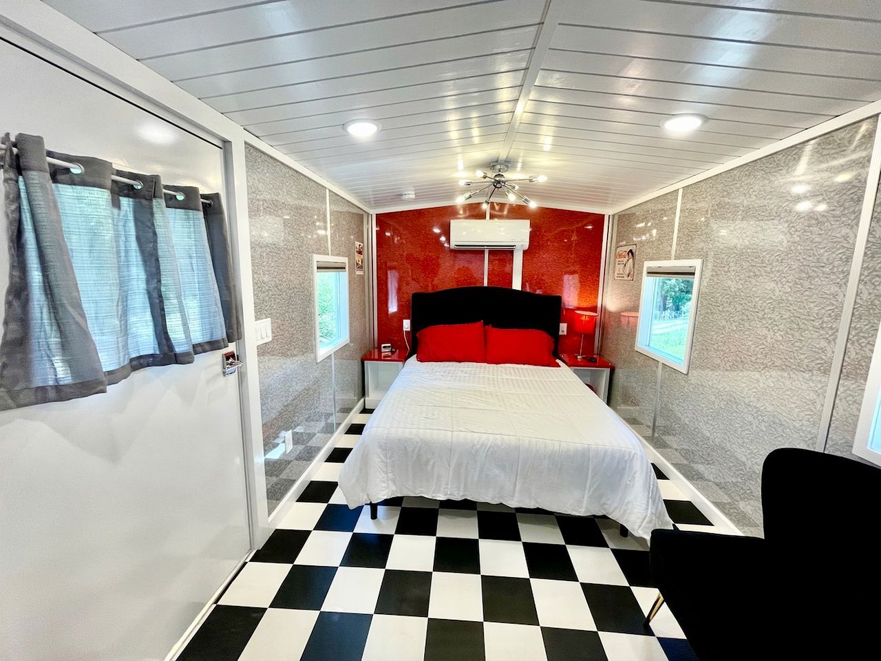 A room with a checkered floor, a bed with white bedding, a red headboard, and a ceiling fan.