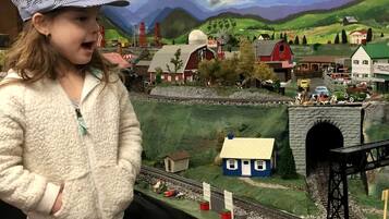 Niño de pie frente a una maqueta de tren con paisaje rural, que incluye un molino, un granero y un puente.