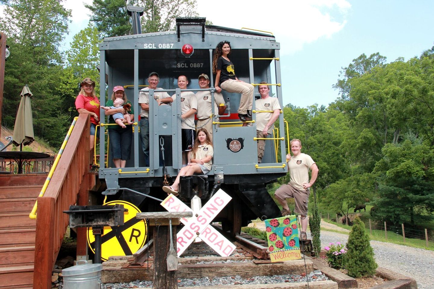 A model train with people posing on it, a wooden platform, and a railroad crossing sign.