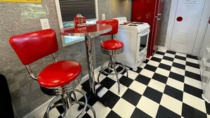 Interior de un restaurante retro con suelo de cuadros, taburetes rojos en la barra, una estufa antigua y un anuncio de Coca-Cola.