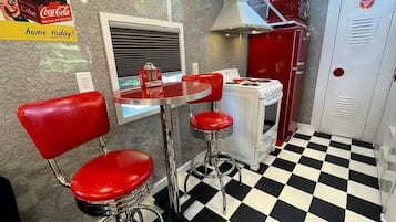 Un interno di una tavola calda d'epoca con pavimento a scacchi, sgabelli da bar rossi, un vecchio forno e una pubblicità di Coca-Cola.