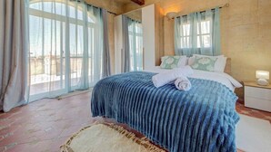 Un dormitorio con una cama grande, una mesita de noche, una lámpara y vistas a través del ventanal.