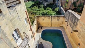 Un patio con piscina, muros de piedra y un pequeño jardín.