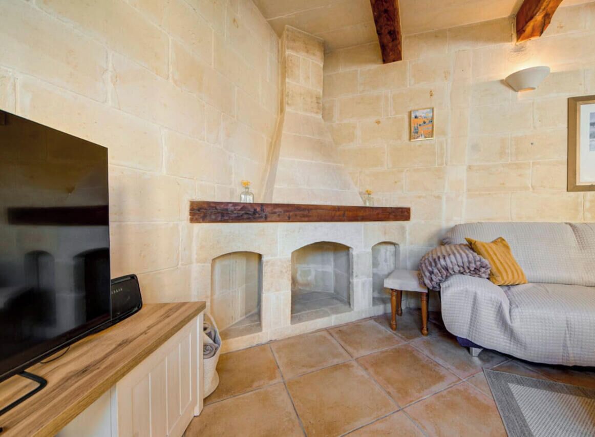 A stone-walled room with a fireplace, a television, and a sofa.