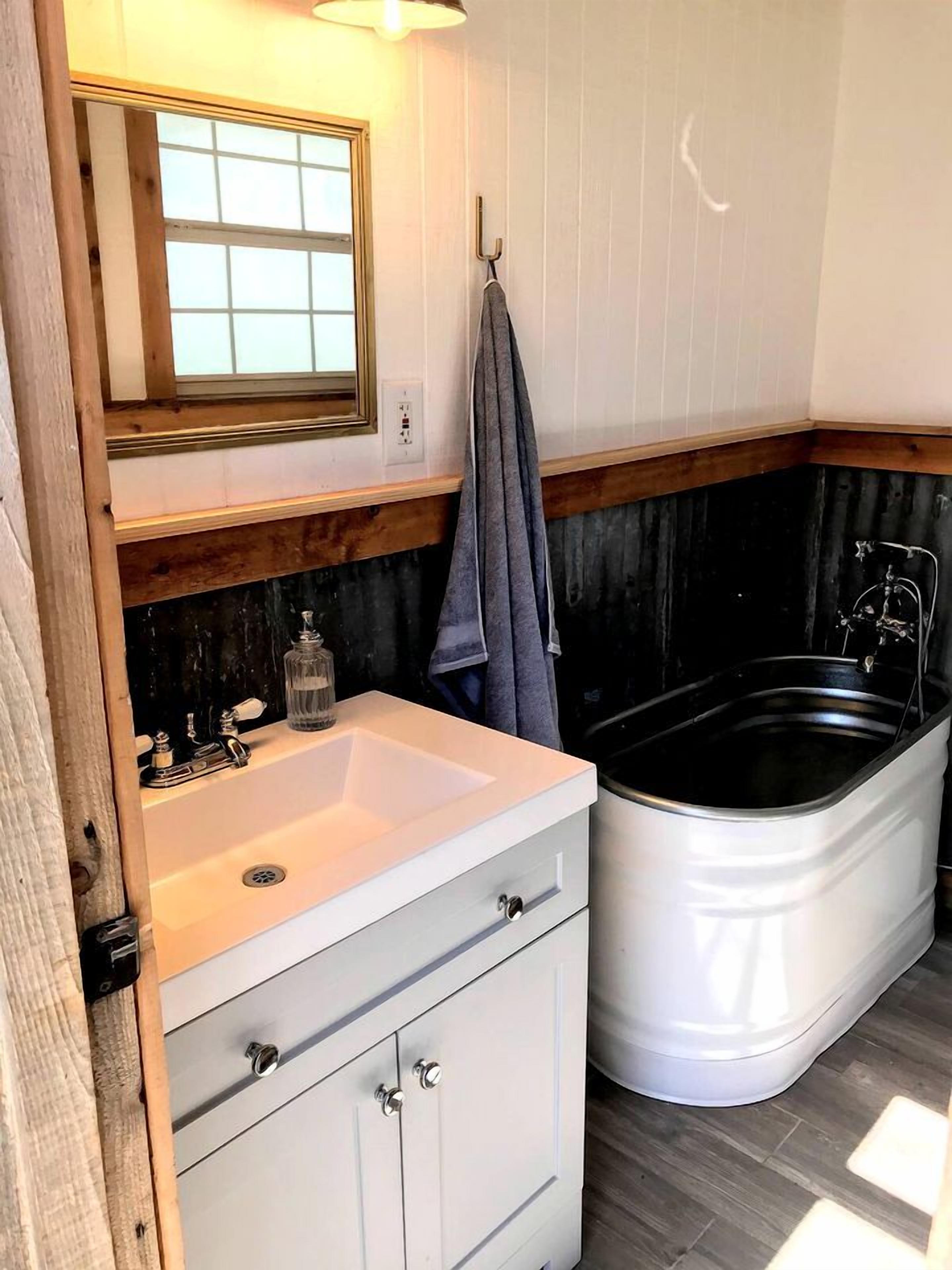 Un baño con lavamanos blanco, espejo, toallero y bañera.