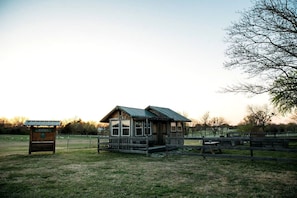 Een rustieke chalet met een metalen dak, omgeven door een omheind gebied met picknicktafels.