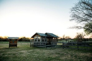 A rustic cabin with a metal roof, surrounded by a fenced area with picnic tables.