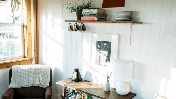 Ein gemütliches Zimmer mit Holzboden, zwei Stühlen, einem Tisch mit Lampe, Büchern und einer Pflanze.