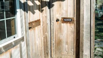 Una porta di legno con un cartello 'WASHROOM', una finestra e un molo in legno con un tappetino d'ingresso.