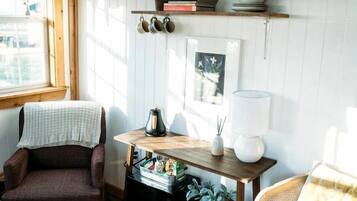 Ein gemütliches Zimmer mit Holzboden, zwei Stühlen, einem Tisch mit Lampe, Büchern und einer Pflanze.