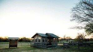 Eine rustikale Holzhütte mit einem Metall-Dach, umgeben von einem eingezäunten Bereich mit Picknicktischen.