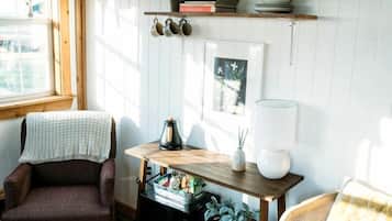 A cozy room with a wooden floor, two chairs, a table with a lamp, books, and a plant.
