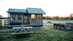 Eine kleine Holzhütte mit einem Metall-Dach, einer Holztür und Fenstern. Vor der Hütte steht ein Picknicktisch.