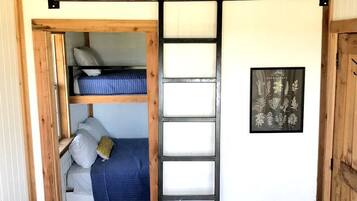 A compact room with a loft bed, a ladder, and a framed botanical print on the wall.