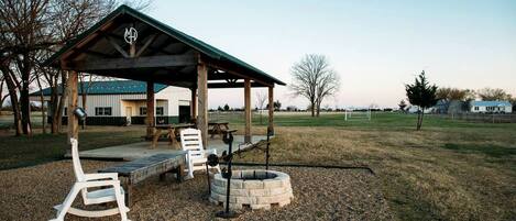 A covered outdoor seating area with a fire pit, a rocking chair, and a picnic table.