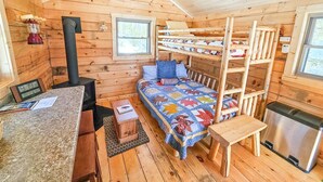 A cozy cabin with a bunk bed, a small kitchen area, a wood-burning stove, and a window.