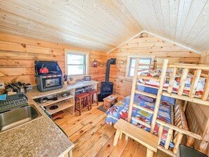 A cabin interior with a kitchen area, a stove, a sink, and a bunk bed.