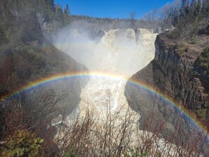 Una cascada amb un arc de sant martí, envoltada de terreny rocos i vegetació escassa.