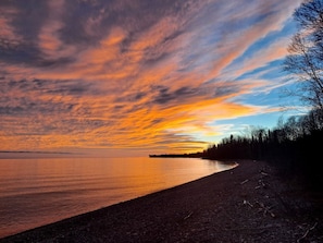 Une plage au rivage incurvé, bordée d’arbres, avec une étendue de terre visible au loin.