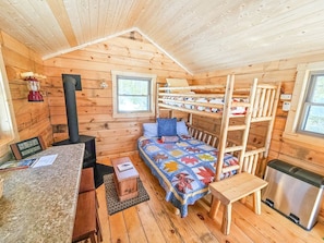 Ein gemütliches Blockhaus mit Etagenbett, einer kleinen Küchenzeile, einem Holzofen und einem Fenster.