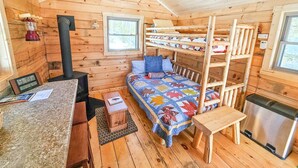 A cozy cabin with a bunk bed, a small kitchen area, a wood-burning stove, and a window. - Cozy Tiny Cabin - Off-Grid Experience with Sled Dogs Year 'round in Minnesota (Grand Marais)