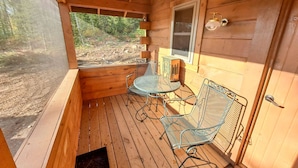 A wooden cabin with a porch, metal chairs, a table, and a window. - Cozy Tiny Cabin - Off-Grid Experience with Sled Dogs Year 'round in Minnesota (Grand Marais)