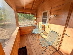 Eine Holzhütte mit Veranda, Metallstühlen, einem Tisch und einem Fenster.