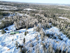 A snow-covered landscape with a building complex featuring multiple structures, surrounded by dense forest.