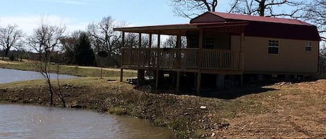 A house with a red roof, a wooden deck, and a pond in the background.