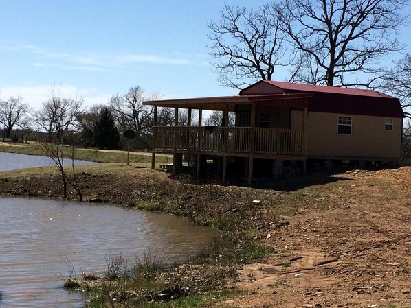A house with a red roof, a wooden deck, and a pond in the background.