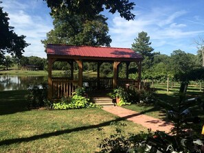 Un pabellón con techo rojo, rodeado por un jardín con estanque y árboles.