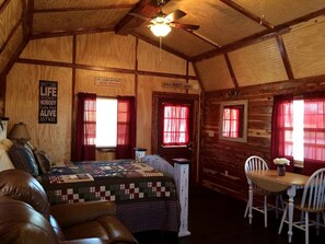 Interior de una cabaña con una cama, una mesa y sillas, y un ventilador de techo.