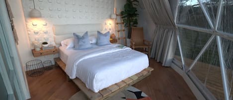 A bedroom with a bed, bedside tables, a lamp, a chair, a window, and a plant.