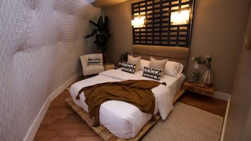 A bedroom with a bed, bedside tables, a wall-mounted light fixture, and a potted plant.
