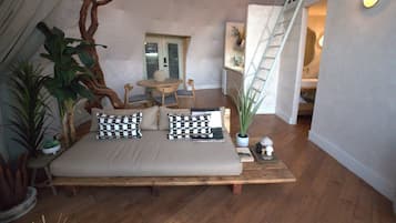 A cozy living area with a sofa, a dining table, and chairs, surrounded by potted plants and a staircase.