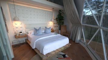 A bedroom with a bed, bedside tables, a lamp, a chair, a window, and a plant.