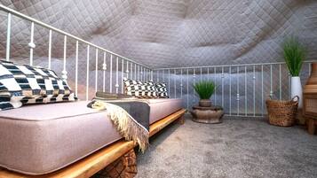 Un dormitorio con cama, un banco, una mesita, una planta en maceta y una cesta decorativa.