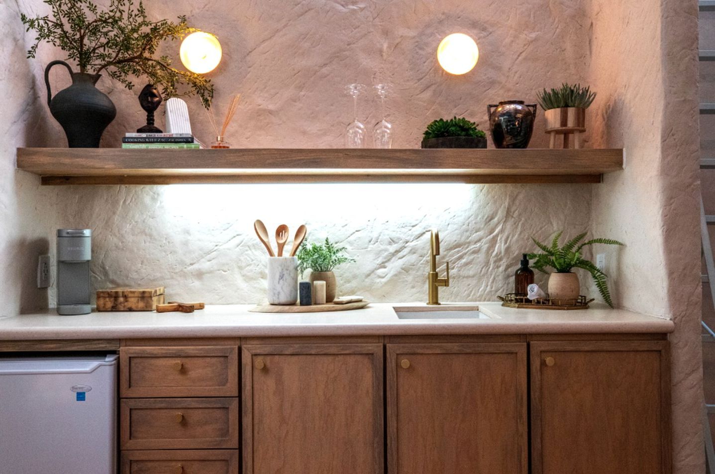 A kitchen with wooden cabinets, a marble countertop, a built-in sink, and a shelf with decorative items.