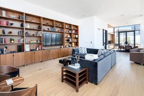 A modern living room with a large bookshelf, a grey sofa, and a flat-screen TV. - Walkable 1BR nr Park Ave & Grand Central (New York)