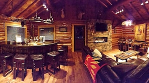 Ein Holzblockhaus-Innenraum mit Barbereich, Sitzgelegenheiten und Kamin.