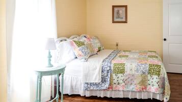 Une chambre à coucher avec un lit, une petite table avec une lampe, une porte et un tableau accroché au mur.